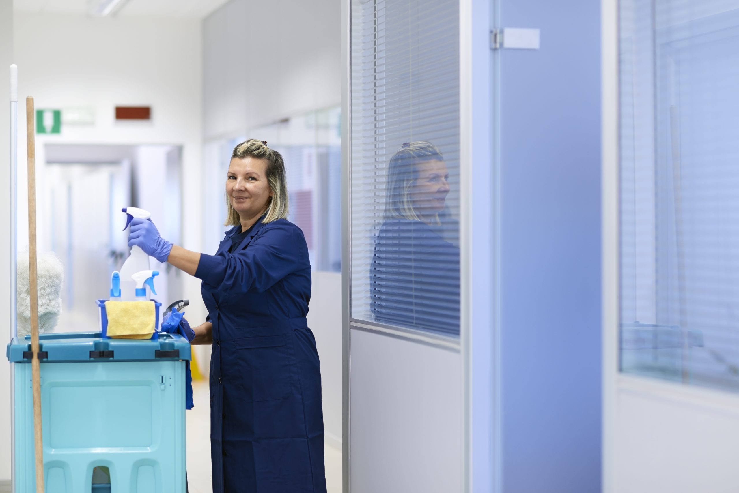 Woman in blue coat professionally cleaning a clinical environment